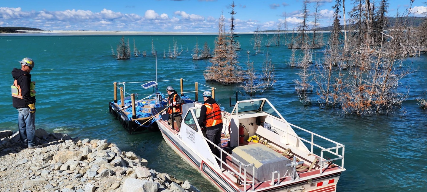 people in boat on shore in large mountain body of water with trees