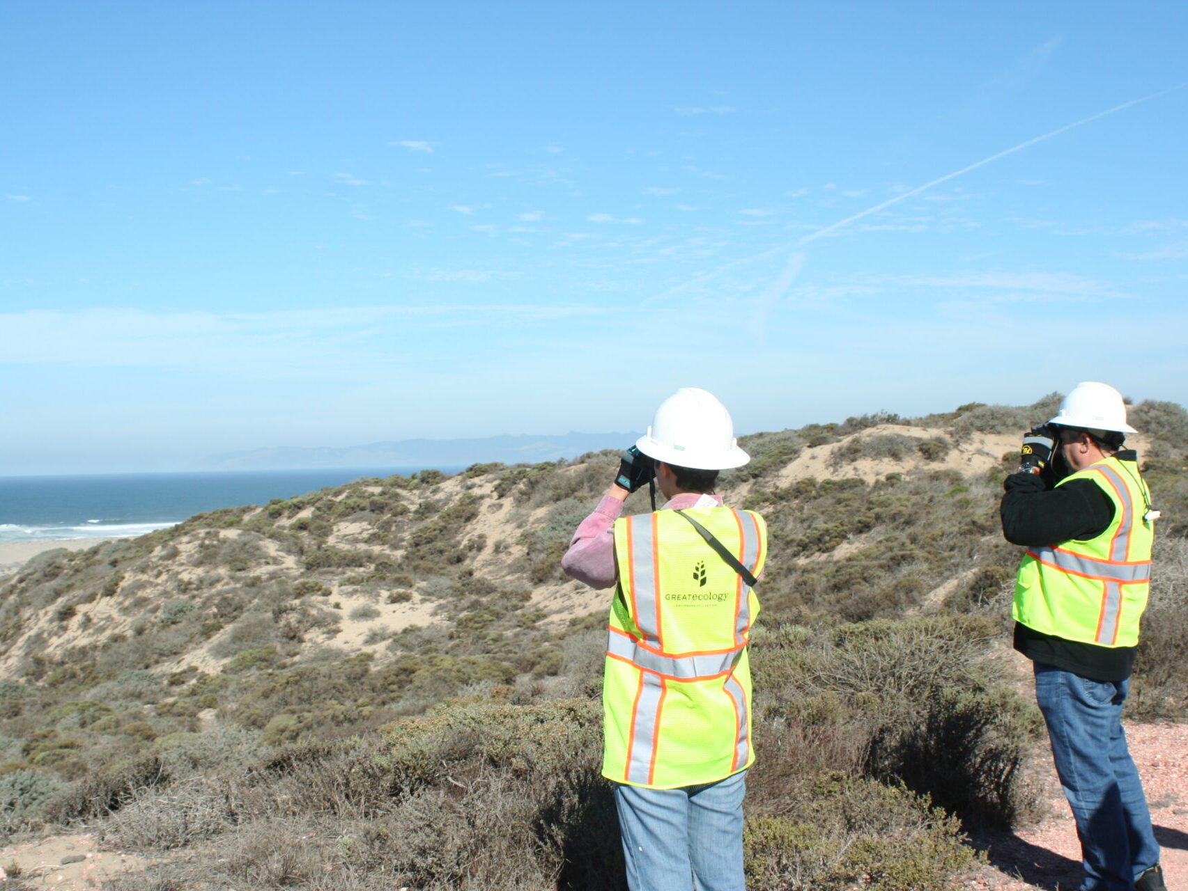 two teams members using binoculars to look out over the coast toward the ocean
