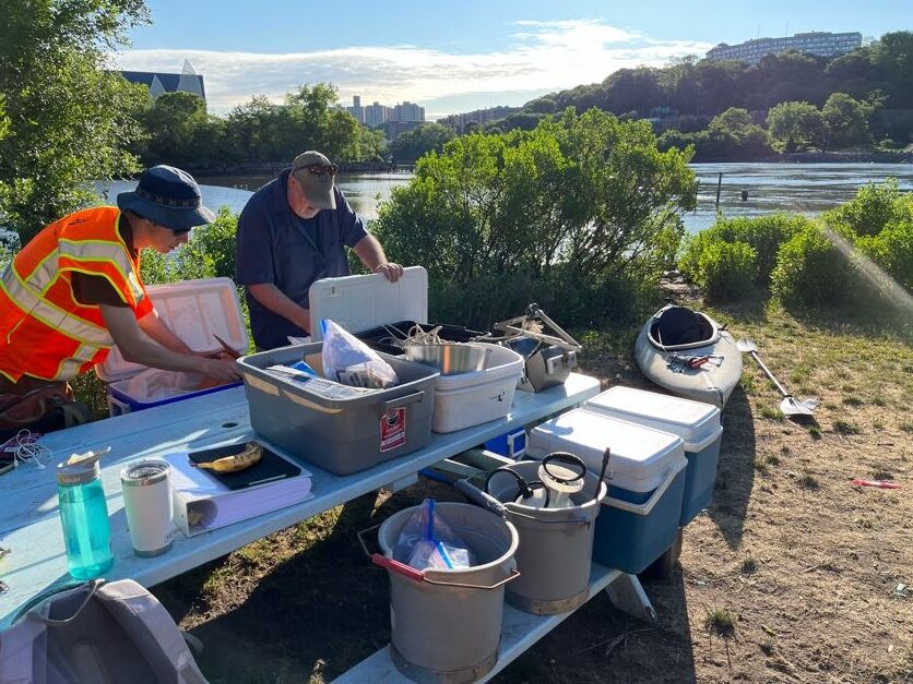 team members laying out supplies on a table on the shoreline with river in the background