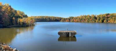 large dam with trees in distance and concrete structure on water