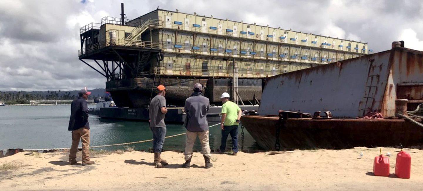 men working on water with damaged structure in distance