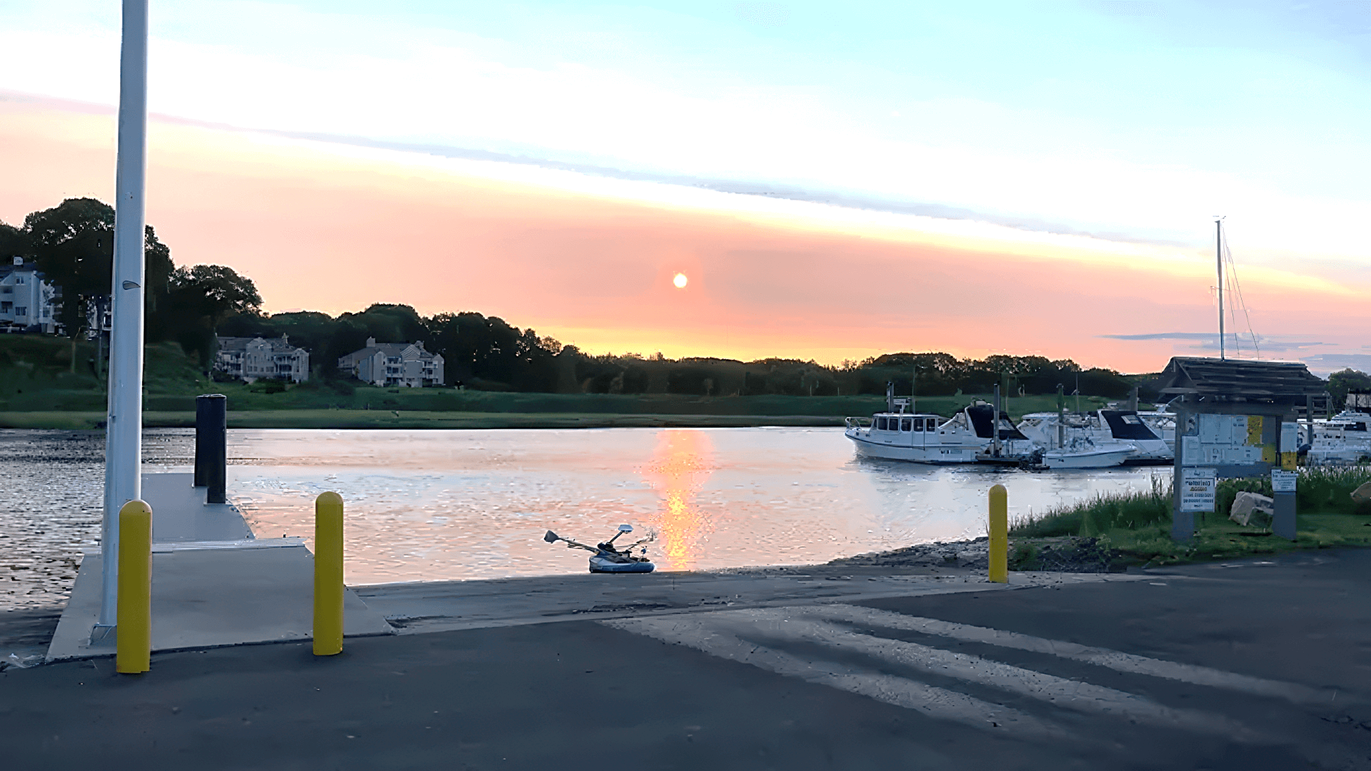 boat launching area of parking lot on river with boats at sunset