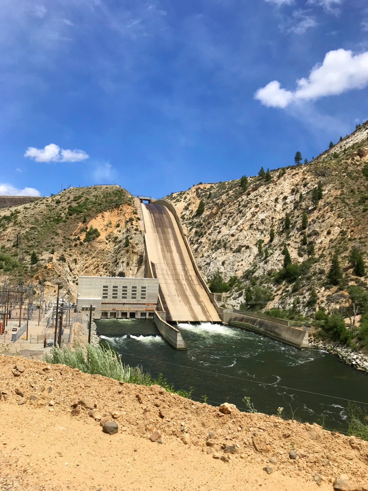 water flow via a dam from top of mountain area into body of water in desert setting