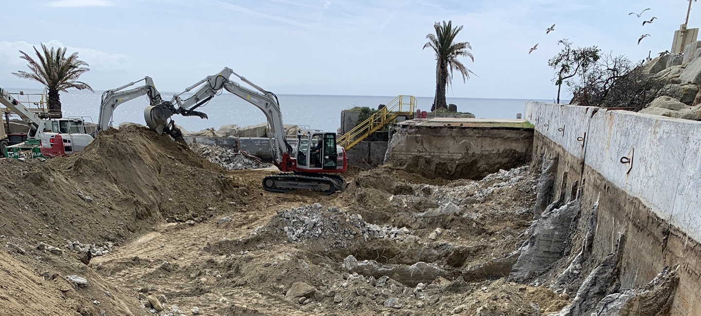 excavator moving dirt in large construction area by the ocean